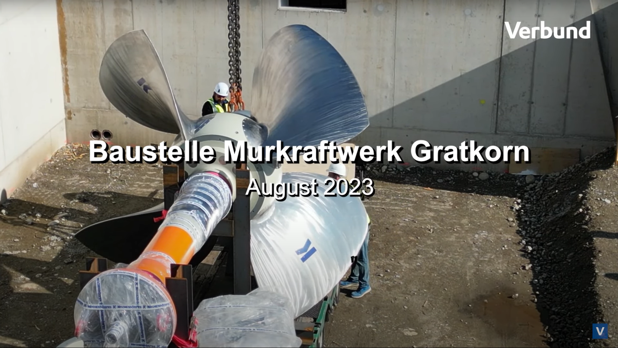 Vorschaubild zum Video über den Turbineneinbau auf der Baustelle Murkraftwerk Gratkorn im August 2023. Zu sehen ist eine große Turbinenschaufel, die mittels Kran angehoben wird, und der stark strukturierte Beton im Hintergrund.